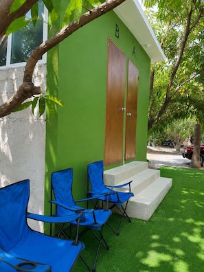 Un edificio verde con dos puertas de madera, unos escalones pequeños y tres sillas plegables azules.