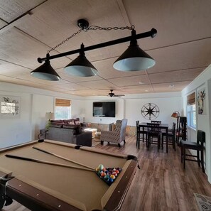 Une table de billard avec des billes, un canapé, une table à manger avec des chaises et un ventilateur de plafond.