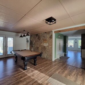 Een pooltafel in een ruimte met houten vloeren, een stenen muur en een deur naar een andere kamer.