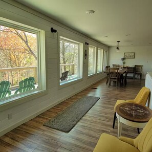 Une pièce spacieuse avec de grandes fenêtres, un plancher en bois et un coin repas comprenant des chaises et une table.