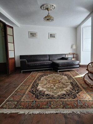 Ein Wohnzimmer mit einer schwarzen Ledersofa, einem gemusterten Teppich, einer Chandelier und gerahmten Bildern an der Wand.