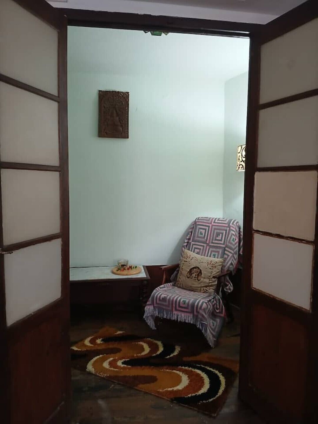 A room with a patterned armchair, a small table with a glass, and a wall-mounted decoration.