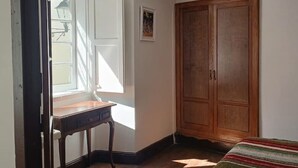 Quarto com guarda-roupa de madeira, cama com manta listrada, escrivaninha e janela com persianas.