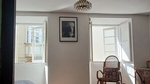 Quarto com tapete estampado, uma poltrona de balanço, um quadro na parede e um lustre.