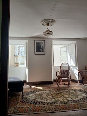 Ein Zimmer mit einem gemusterten Teppich, einem Schaukelstuhl, einem gerahmten Bild an der Wand und einer Kristallleuchtre.