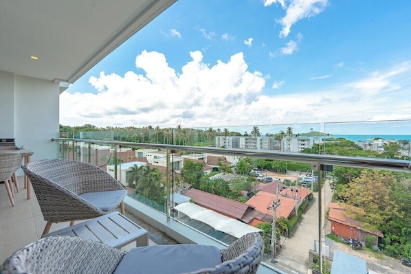A balcony with wicker furniture, a clear view of the ocean, and surrounding buildings.