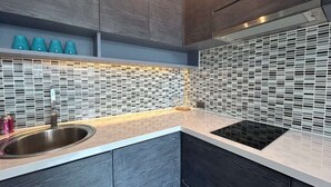 Una cocina moderna con un lavamanos de acero inoxidable, una placa de inducción negra y un salpicadero con un diseño de mosaico.