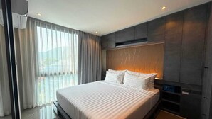 Una habitación de hotel moderna con una cama grande, un televisor integrado y vistas al exterior.