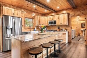 A spacious kitchen with wooden cabinetry, a stainless steel refrigerator, a microwave, and a large island with bar stools. - Stunning Views! Firepit/Hot Tub/Games&Theater Room (Sevierville)