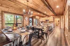 A wooden cabin interior with a dining area, kitchen, and large windows. - Stunning Views! Firepit/Hot Tub/Games&Theater Room (Sevierville)