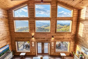 A cabin with multiple large windows offering mountain views, a wooden interior, and a deck with outdoor seating. - Stunning Views! Firepit/Hot Tub/Games&Theater Room (Sevierville)