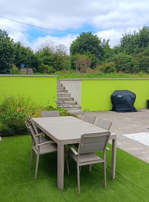 Eine Terrasse mit Tisch und Stühlen, einer grünen Wand und einer Treppe zu einer erhöhten Ebene.