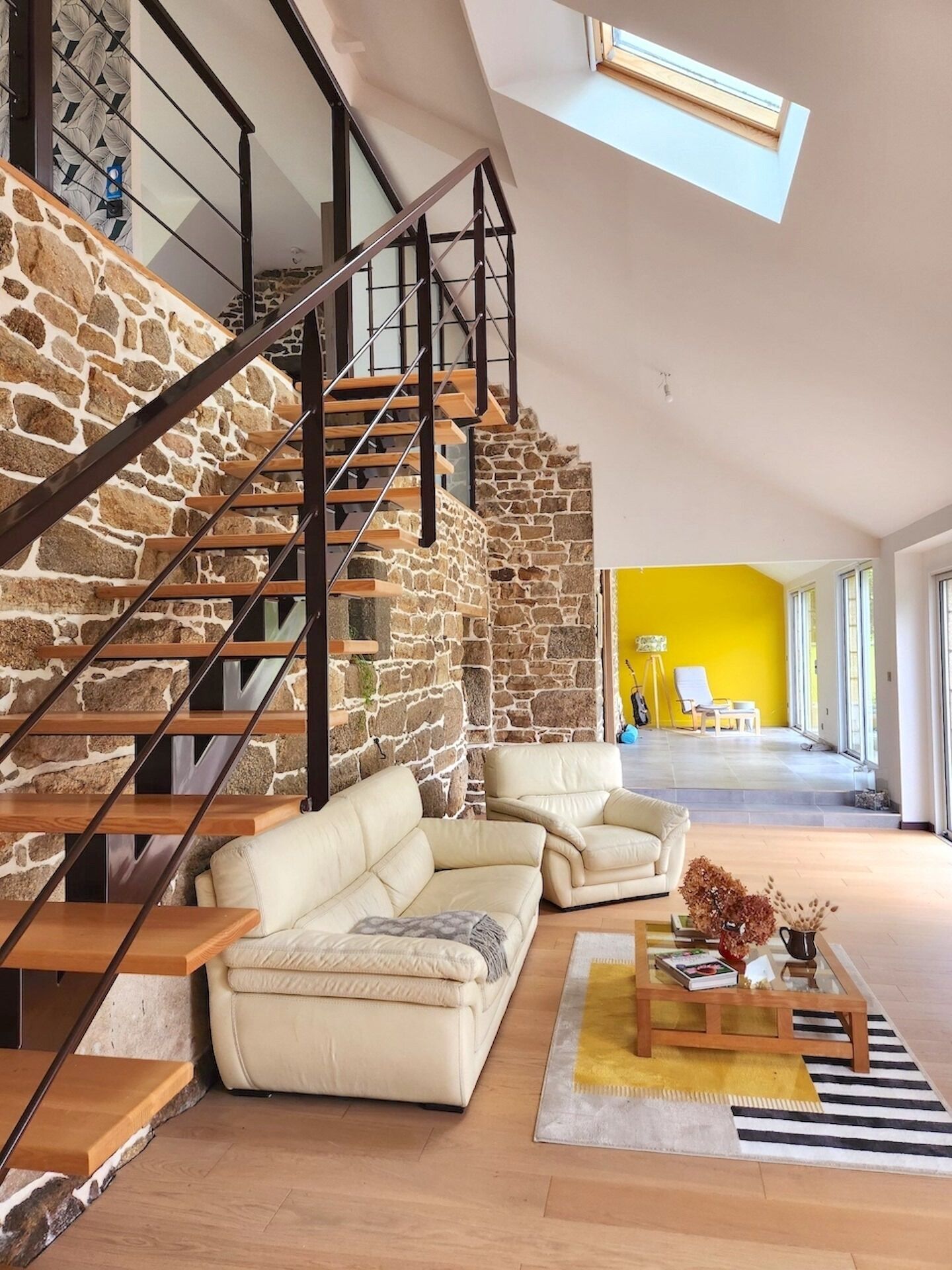 A modern living space with a stone staircase, leather sofas, and a bright yellow wall.