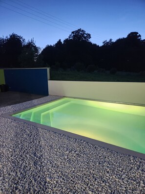 Ein Schwimmbecken mit Kiesbord, umgeben von einer niedrigen Mauer und wolkenlosem Himmel.