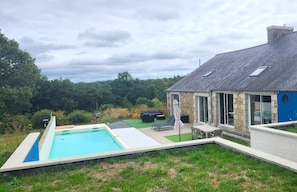 Ein Wohnhaus mit Swimmingpool, Sitzgelegenheit im Freien sowie ein Steinhaus mit großen Fenstern.