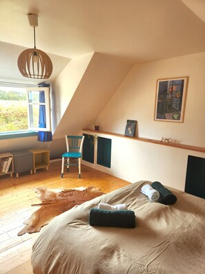A bedroom with a sloped ceiling, a bed with pillows, a chair, a desk, and a window with curtains. - An authentic, renovated Breton house. Perfect for recharging!   (Lanvellec)