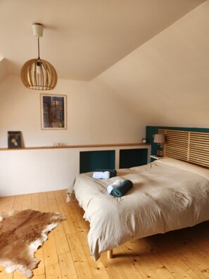 Ein Schlafzimmer mit Bett, Holzboden, einer Hängeleuchte, einem gerahmten Bild an der Wand und einem Fellteppich.