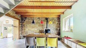 Uma área de refeições com parede de pedra, teto de madeira e uma mesa com cadeiras.