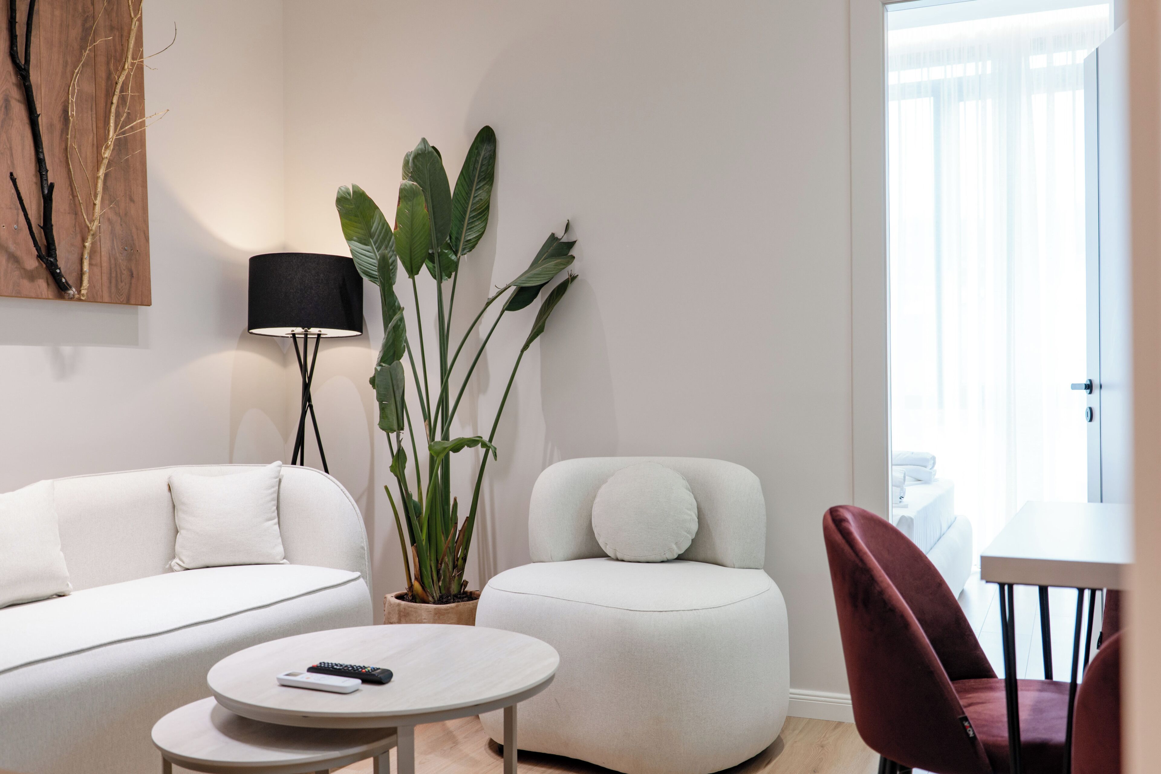 A modern living room with a sofa, a round coffee table, a red chair, a potted plant, and a lamp.