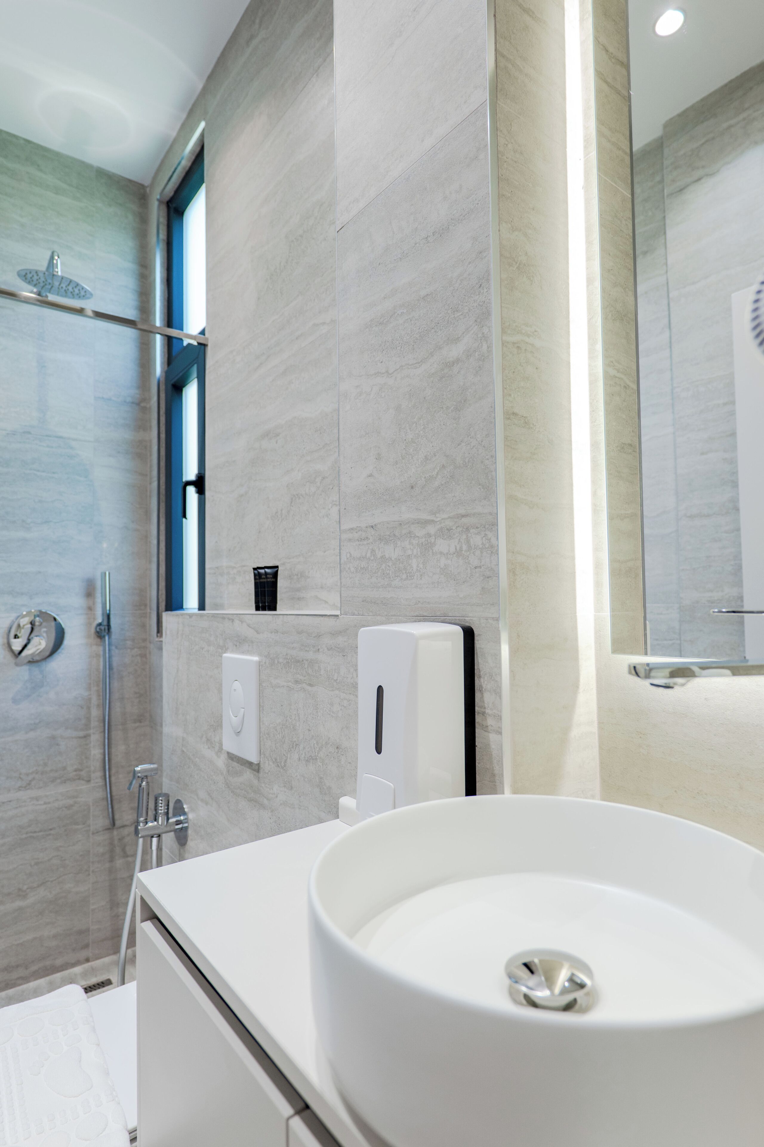 A modern bathroom with a large sink, a shower, and a mirror.