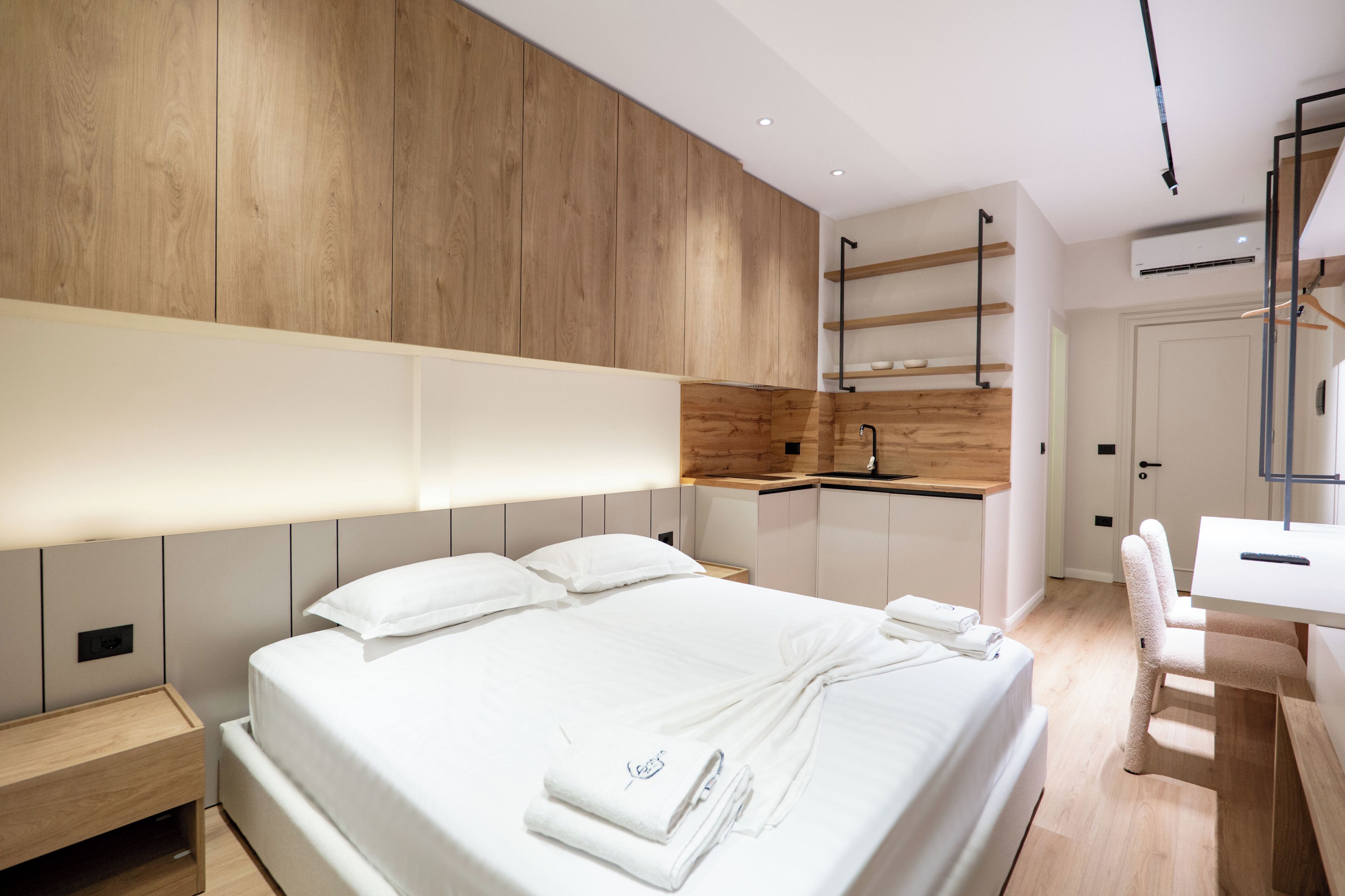 Ein modernes Hotelzimmer mit einem großen Bett, einer Wand mit Holzpaneelen, einer Küchenzeile und einem Schreibtisch mit Stuhl.