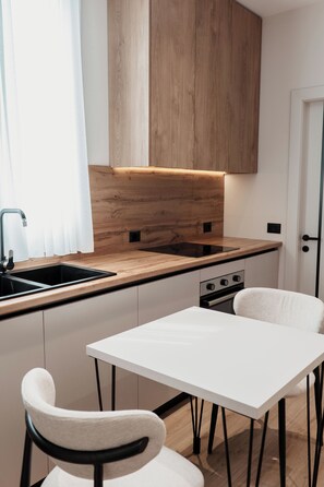 Eine moderne Küche mit Holzausbau, einer weißen Arbeitsplatte, einer Spüle, einem Ofen und einem weißen Tisch mit zwei Stühlen.