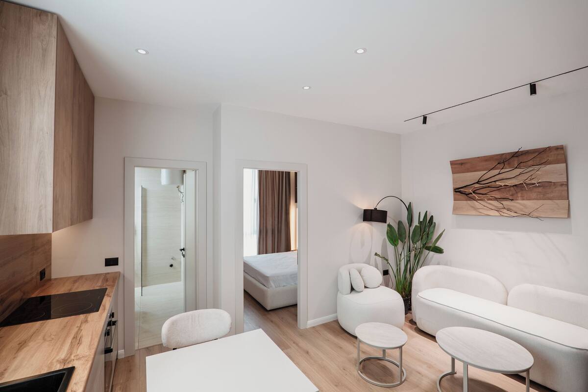 A modern hotel room with a kitchenette, a sofa, a dining table, and a bed.
