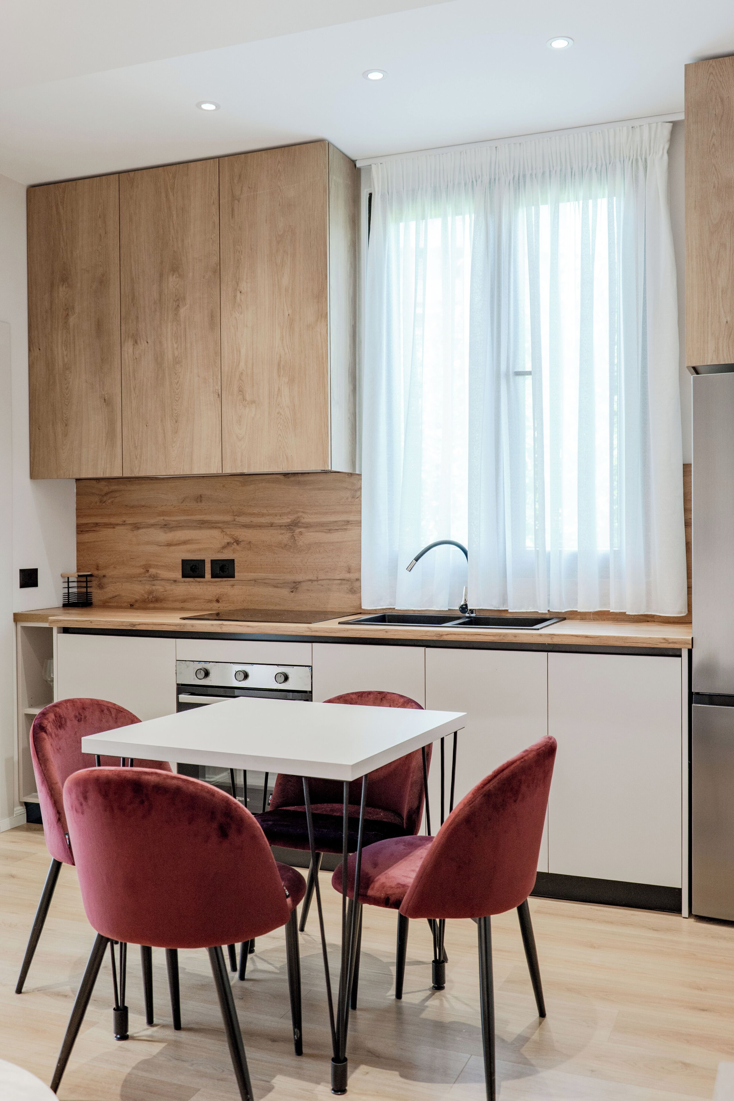 Een moderne keuken met houten kastjes, een wit aanrecht, een roestvrijstalen spoelbak en een eettafel met vier stoelen.