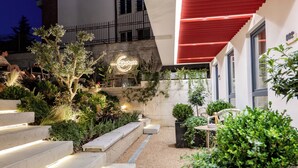 A modern outdoor area with steps leading to a seating area, a sign reading 'Gatum,' and a building with a red awning.