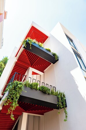 Un edificio moderno con fachada roja y blanca, una escalera y plantas verdes en balcones.