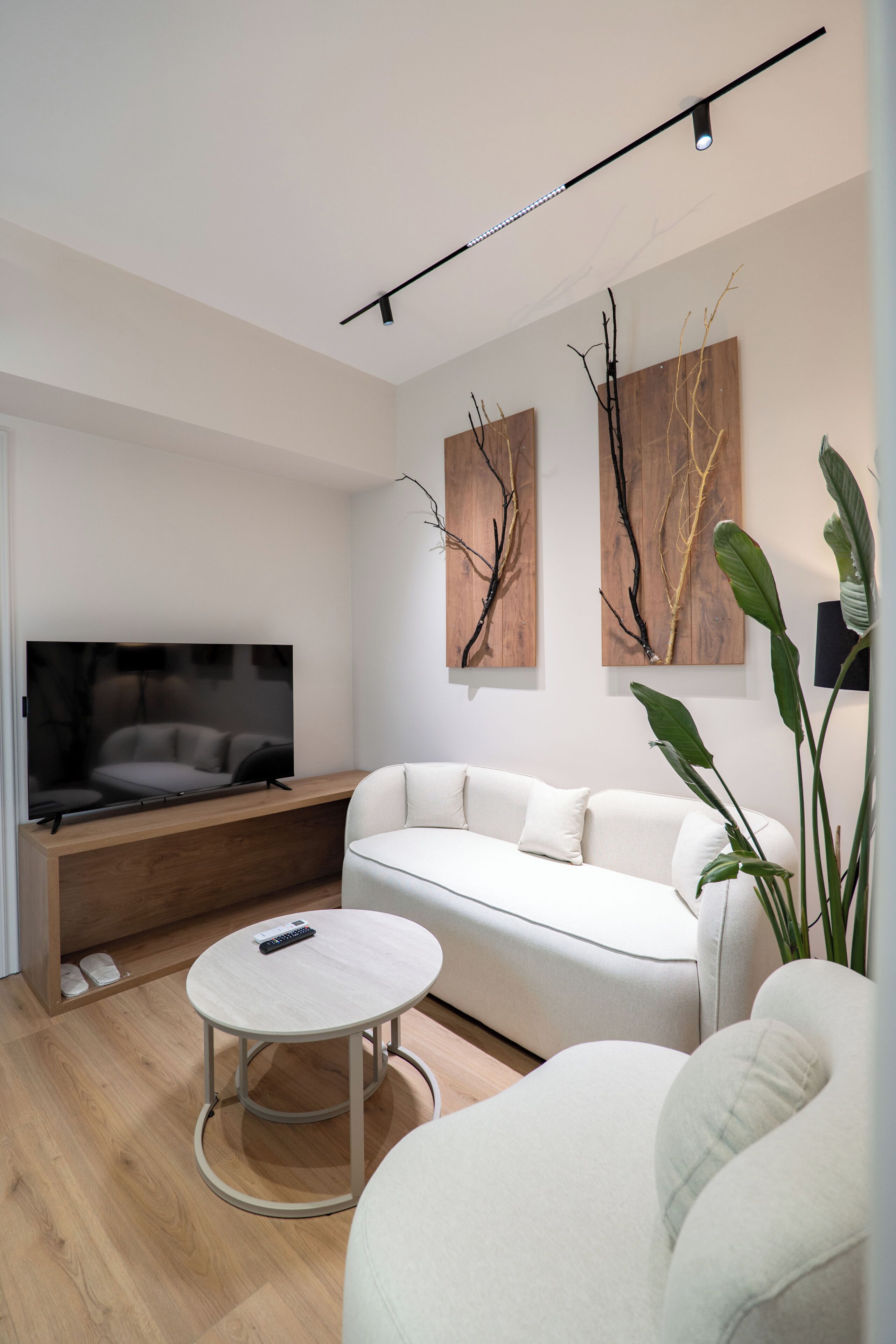 A modern living room with a flat-screen TV, white sofa, round coffee table, and artwork on the wall.