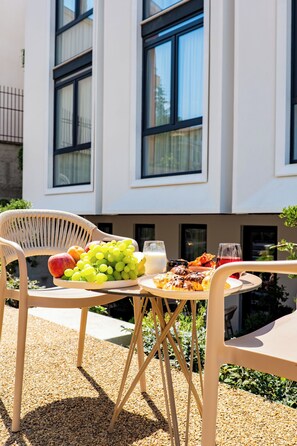 Una mesa de comedor con un plato de frutas, vasos y un plato de comida, ubicada al aire libre con un edificio de fondo.