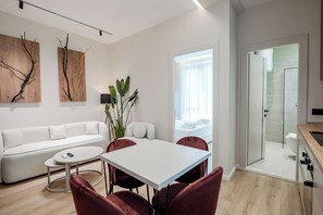 Una sala moderna con un sofá blanco, una mesa de comedor con sillas y una cocina visible a través de una puerta abierta.