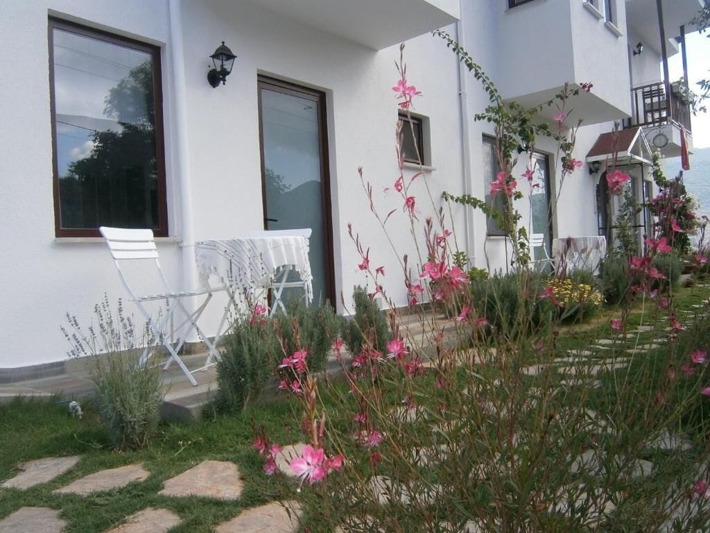 A white building with large windows, a balcony, and a garden with pink flowers.