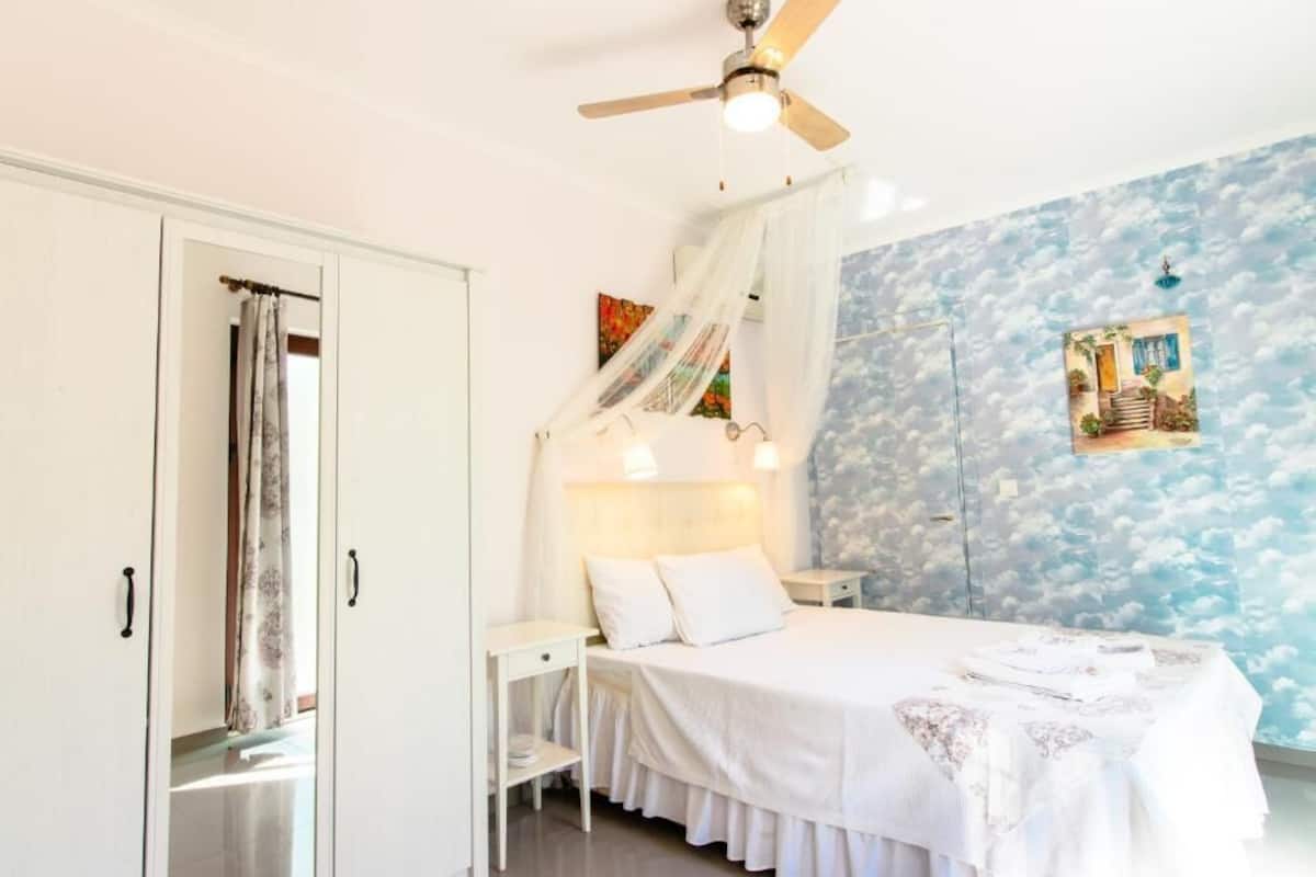 A bedroom with a bed, a nightstand, a ceiling fan, and a wall with a cloud pattern.