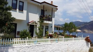 A two-story building with a balcony, a white picket fence, and a view of a lake and mountains. - Masal Tatil Evi  (Marmaris)