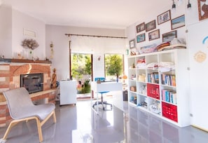 Un salón con chimenea, una estantería y vistas al exterior.