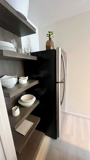 Eine Küche mit einem schwarzen Kühlschrank, weißen Regalen und einer kleinen Pflanze darauf.