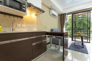 Eine moderne Küche mit Mikrowelle, Herd und Spüle, eine Bar mit Barhocker und ein Balkon mit Blick auf Palmen.