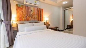 A hotel room with a bed, bedside lamps, a painting on the wall, an air conditioning unit, and a mirror. - MBC MaiKhao 1BR Condo•Poolside•Walk 2 Beach C194 (Tambon Mai Khao)