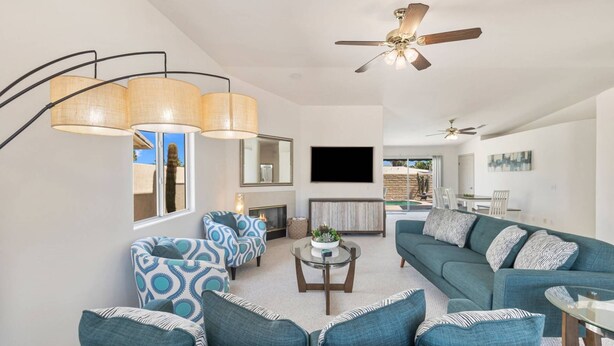 A living room with a ceiling fan, a TV mounted on the wall, and a fireplace. - South Palm Desert Home with Private Pool, 3-Car Garage & Close to El Paseo (Palm Desert)