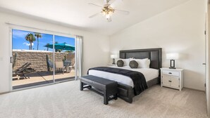A bedroom with a bed, bedside tables, a ceiling fan, and a view of an outdoor patio with chairs and a table. - South Palm Desert Home with Private Pool, 3-Car Garage & Close to El Paseo (Palm Desert)