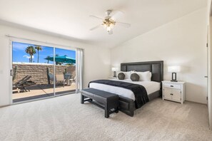 Ein Schlafzimmer mit Bett, Nachttischen, Deckenventilator und Blick auf eine Terrasse mit Stühlen und Tisch.