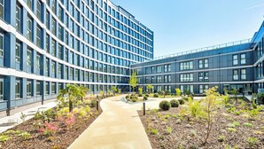 A modern building with a curved facade, a central pathway, and landscaped areas with various plants. - 4-Guest North London | Piccadilly Line into Zone 1 (Barnet)