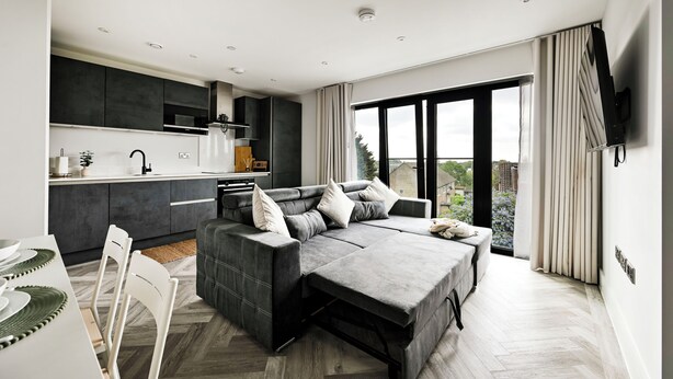 A modern living space with a sofa, dining table, and kitchen area. - 4-Guest North London | Piccadilly Line into Zone 1 (Barnet)