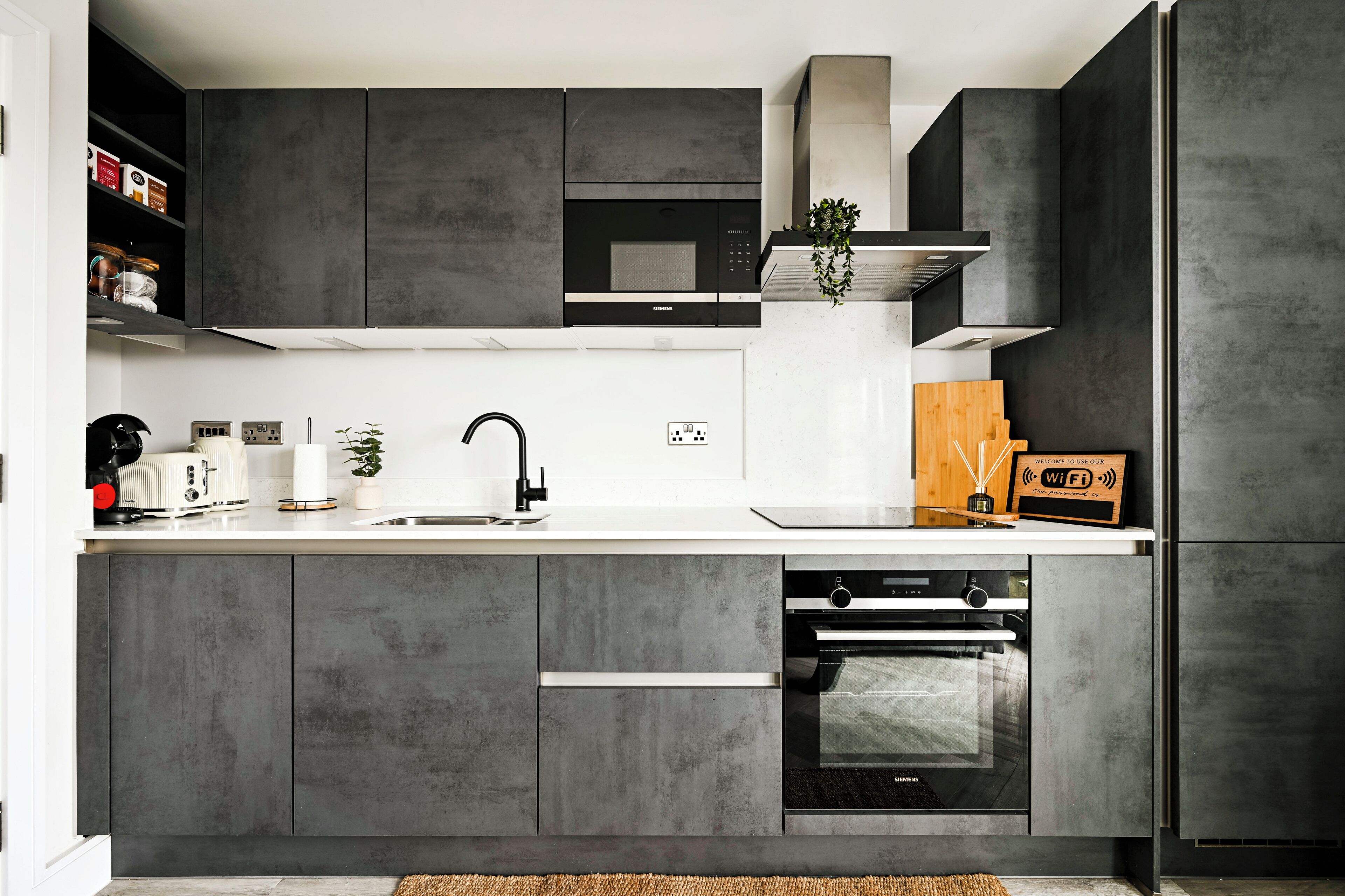 A modern kitchen with grey cabinetry, a built-in microwave, an oven, and a white countertop.