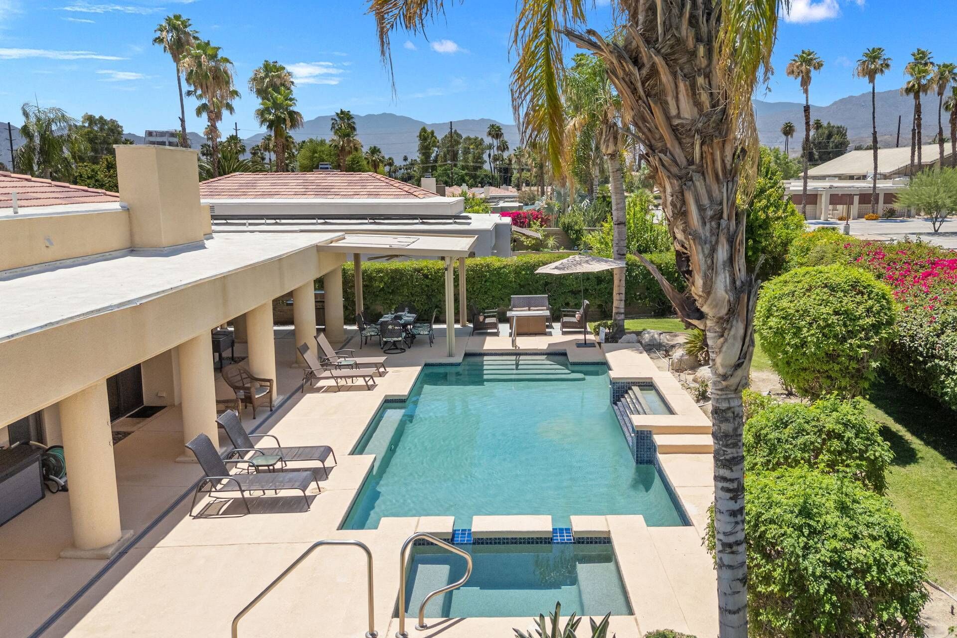 A pool area with lounge chairs, a covered seating area, and a view of mountains in the background.