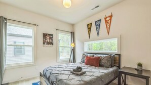 Ein Schlafzimmer mit einem Bett, einem Schreibtisch und zwei Fenstern. An der Wand hängen drei Wimpel.