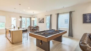 Ein modernes Wohnzimmer mit Billardtisch, Küchenzeile und Essbereich.