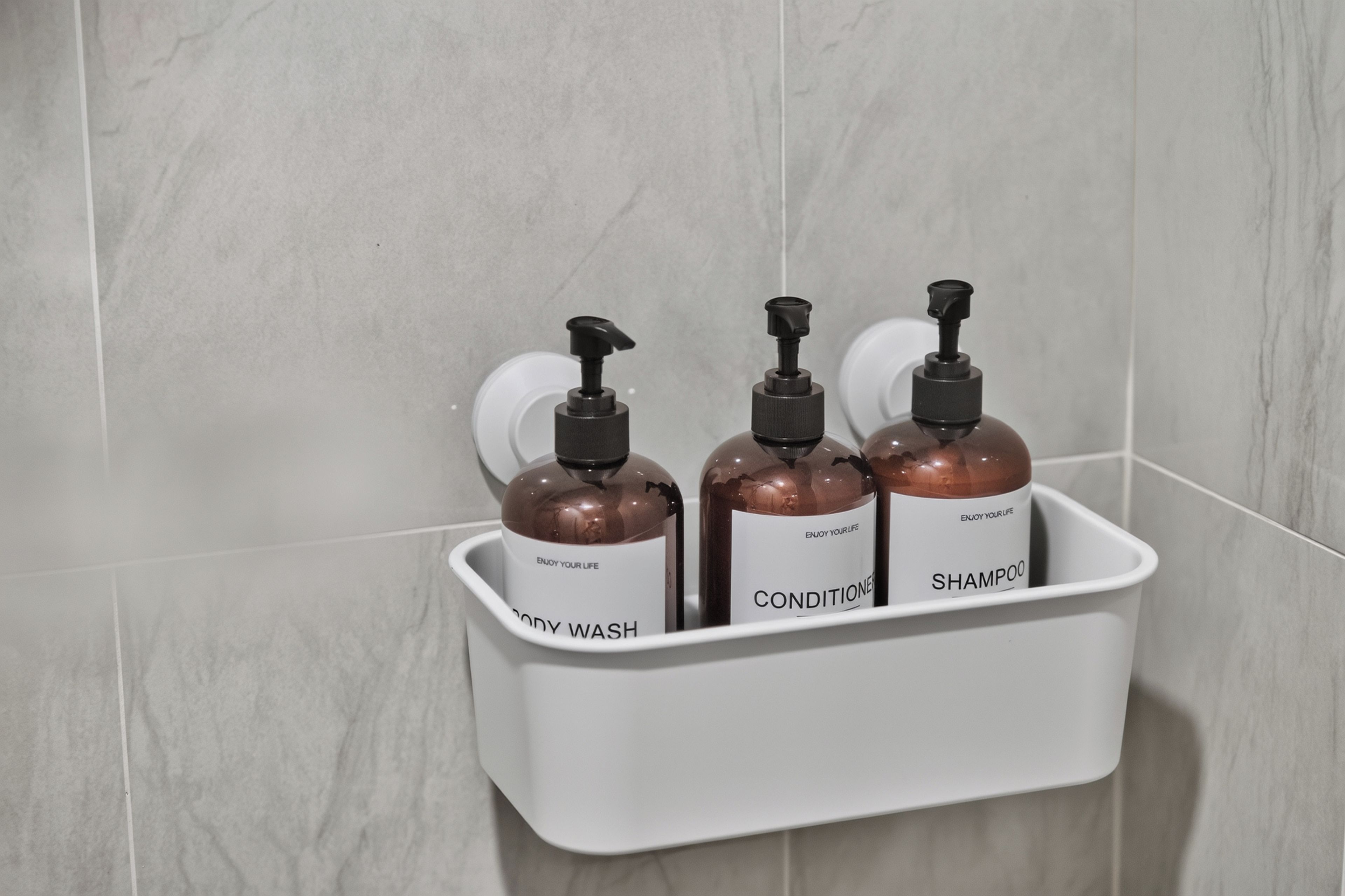 A bathroom shelf with three bottles of shampoo and conditioner.